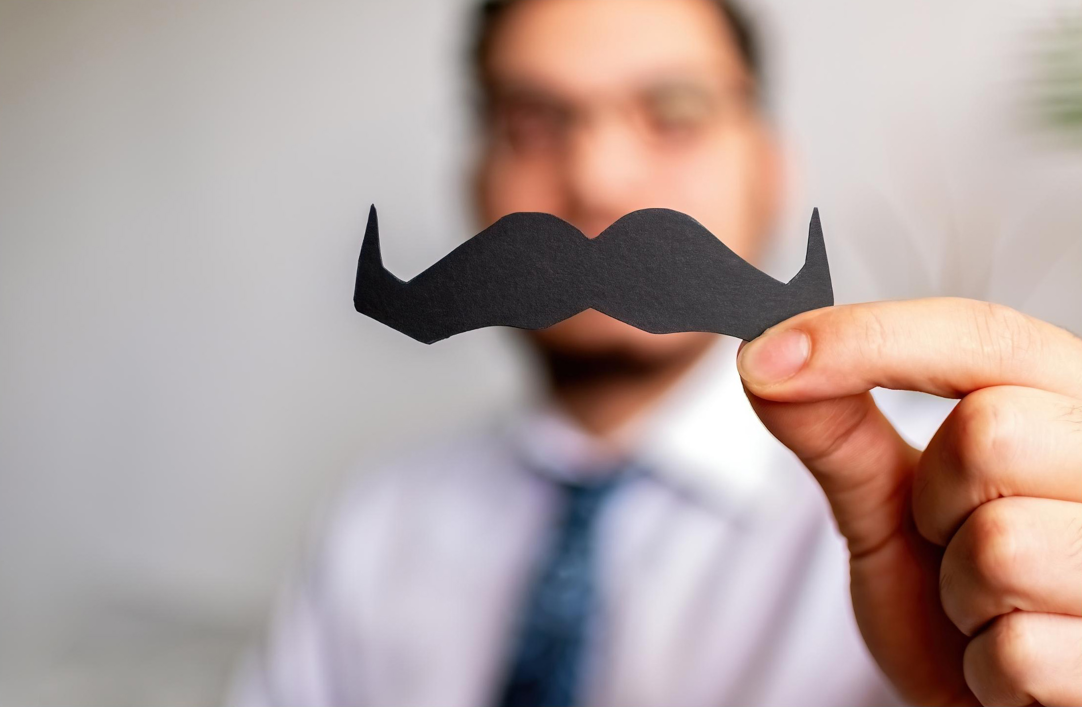 Man in suit holding paper moustache